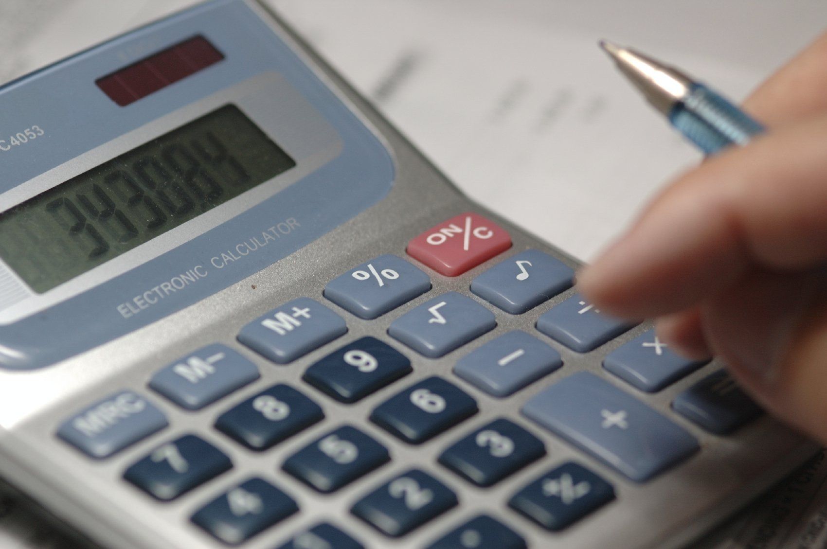 Imagem mostra uma calculadora e dedo de um homem fazendo contas