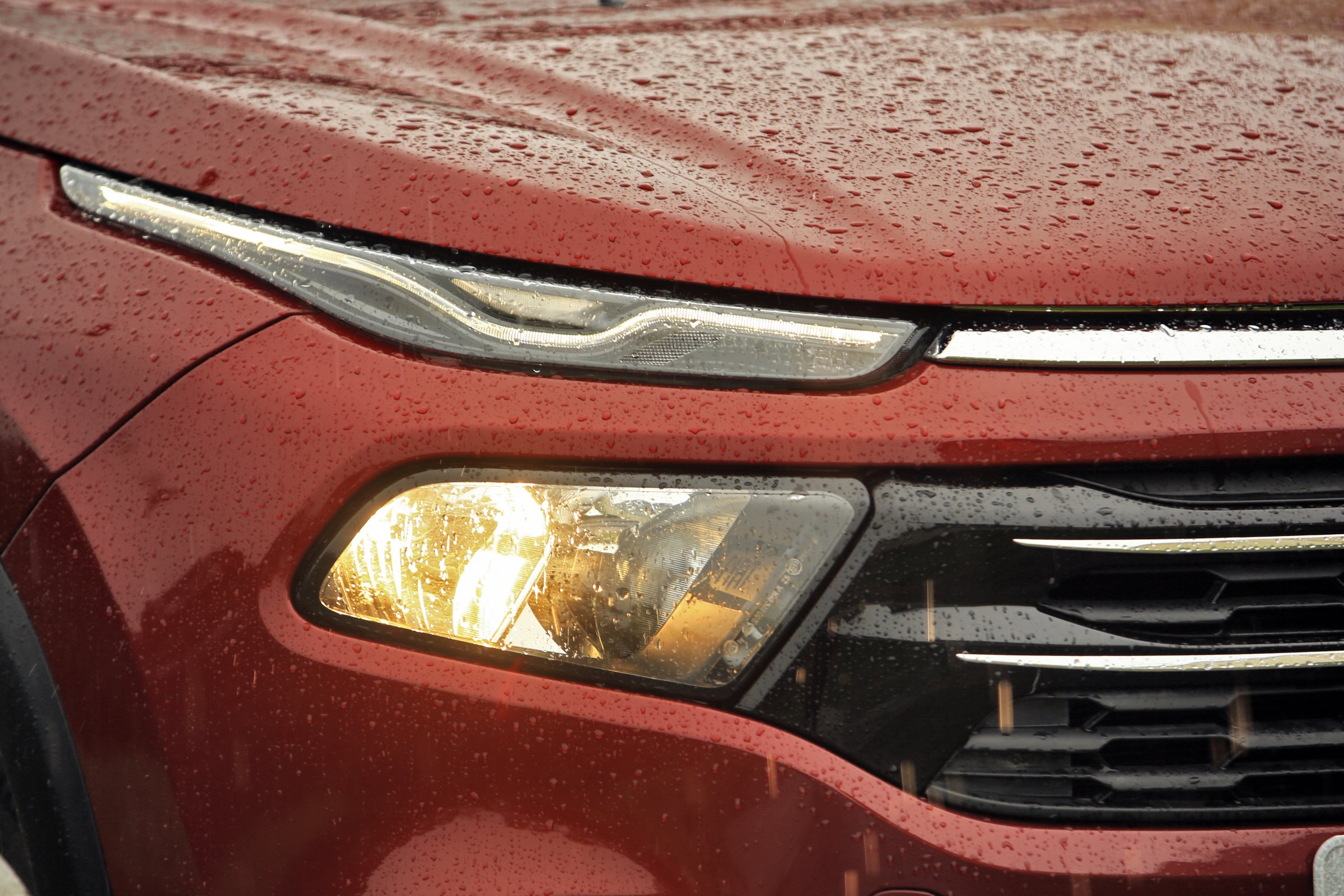 Detalhe do farol da Fiat Toro 2.4 TigerShark vermelha com capô molhado de chiva e farol de neblina aceso