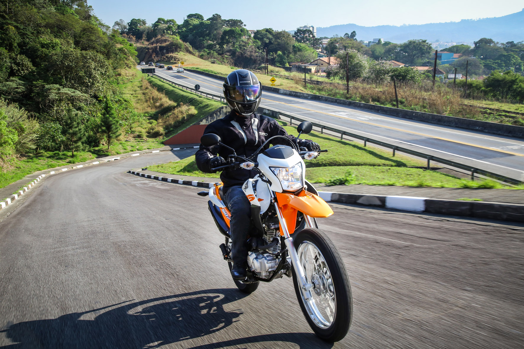 Bros 160 CBS na cor laranja subindo uma ladeira com estrada ao fundo