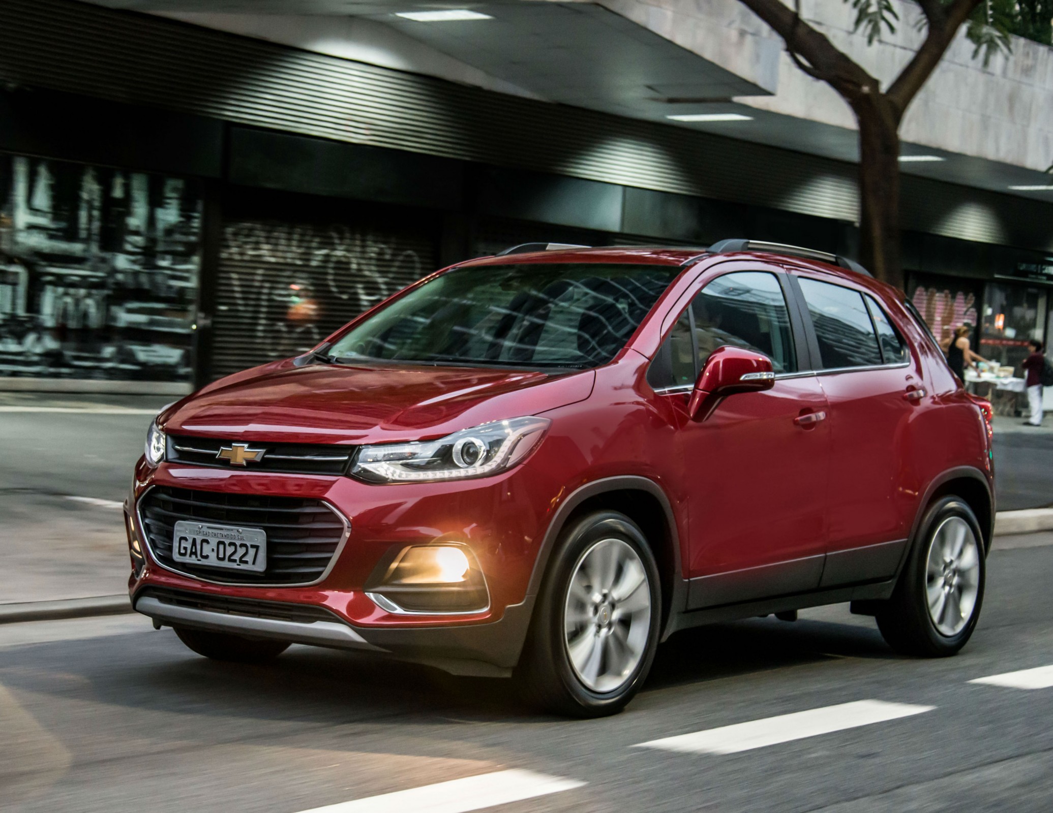 Chevrolet Tracker Premier na cor vinho em movimento na rua e com os faróis acesos