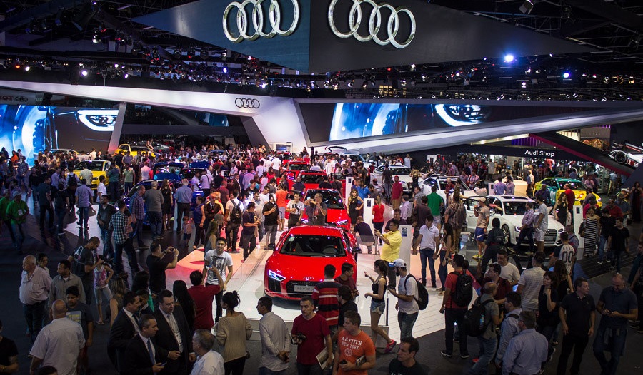 Foto aberta do Salão do Automóvel de 2018 com várias pessoas em torno d eum caro vermelho em exposto no estande da Audi