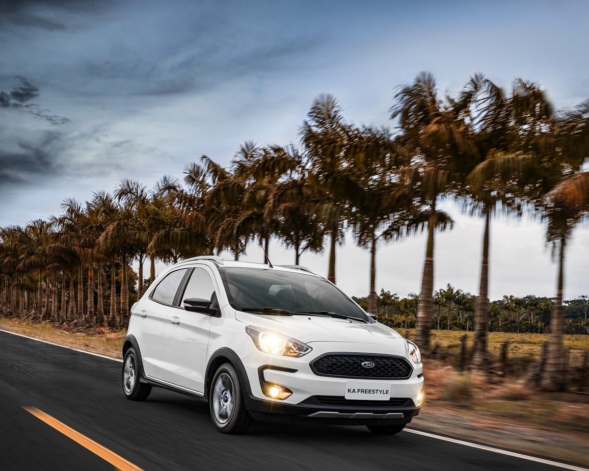 Ford Ka Freestyle branco em movimento numa estrada no litoral margeada por palmeiras e ao fundo a praia