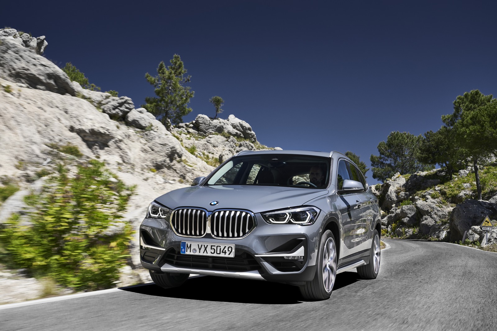 BMW X1 em movimento tendo uma pedra branca ao fundo de uma curva na estrada