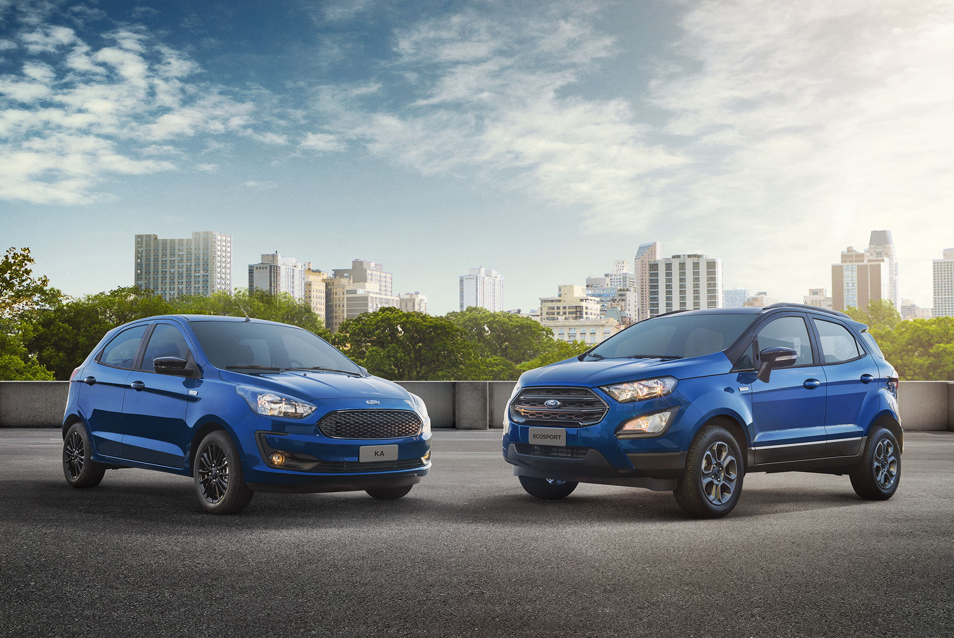 Ford Ka e EcoSport azuis frente a frente em um estacionamento com ao funcdo prédios e céu azul
