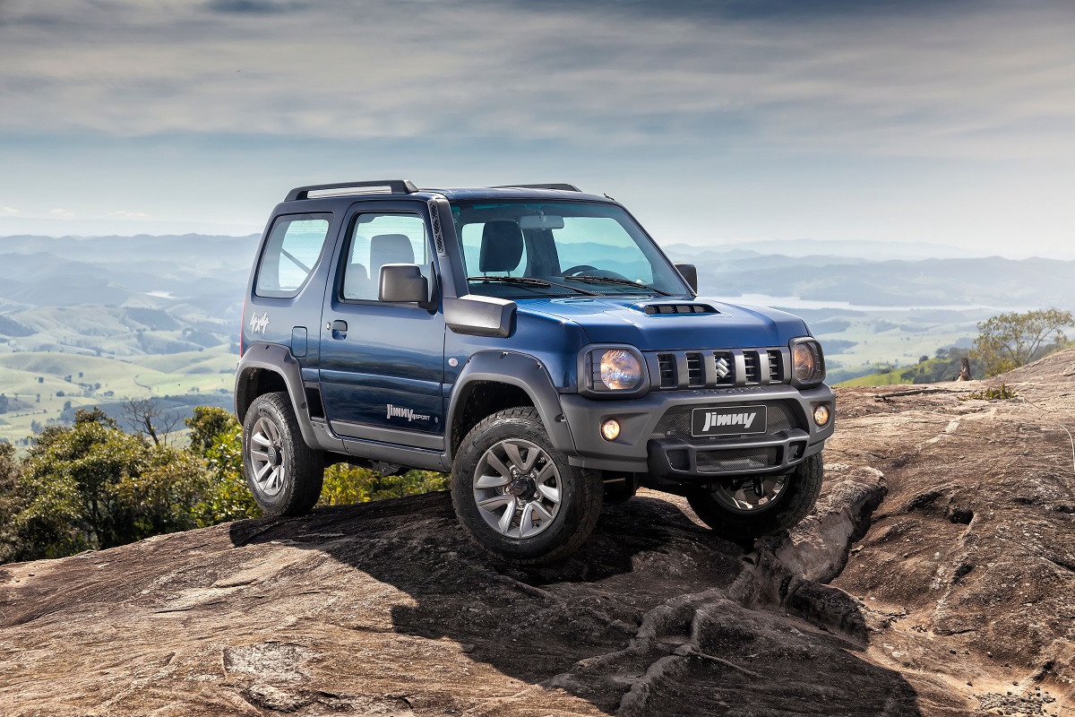 Suzuki Jimny azul no alto de uma pedra ao fundo um vale com montanhas ao longe