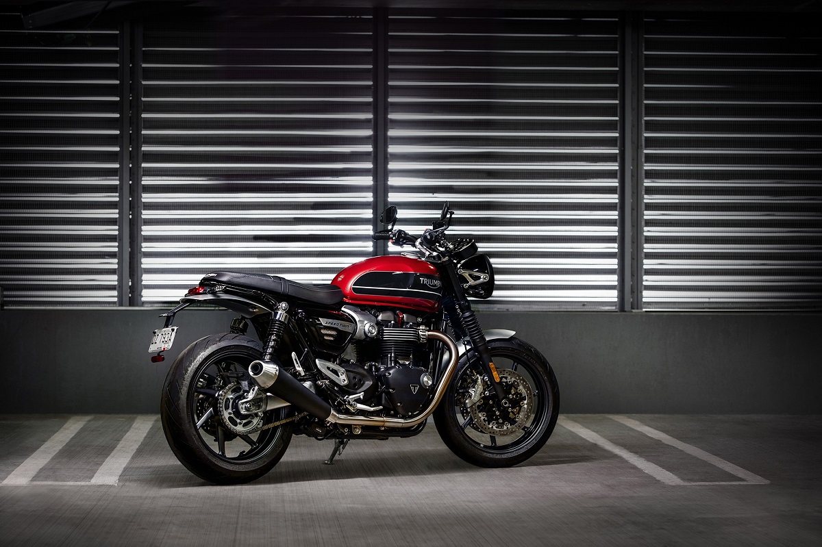 Triumph Speed Twin com tanque vermelho de perfil em uma garagem ao fundo uma porta pantográfica