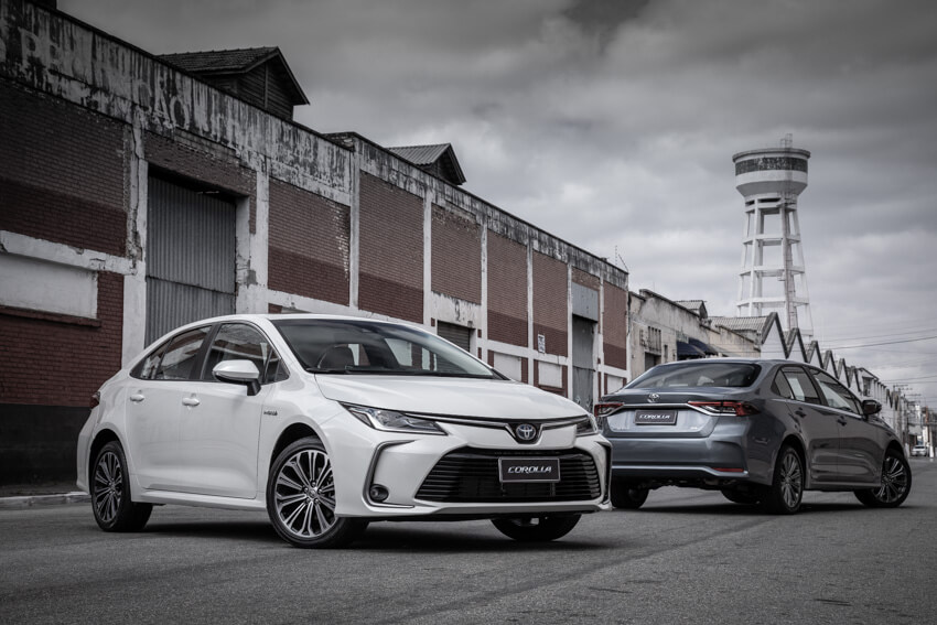 Toyota Corolla Híbrido de frente na cor branca tendo ao fundo um galpão