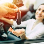 mulher sorrindo dentro do carro enquanto recebe a chave do automóvel