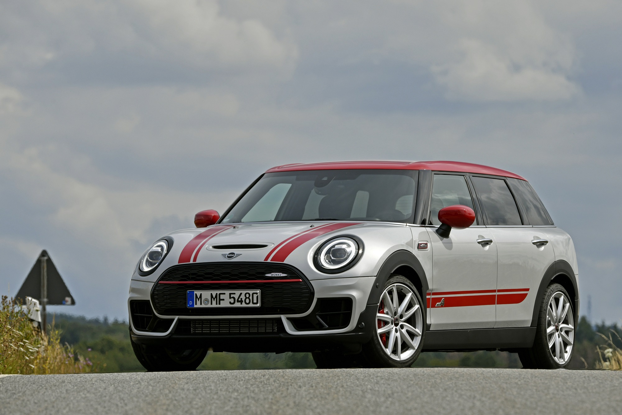 Mini Clubman na cor prateada de frente com os tradicionais faróis redondos e faixas vermelhas sobre o capô