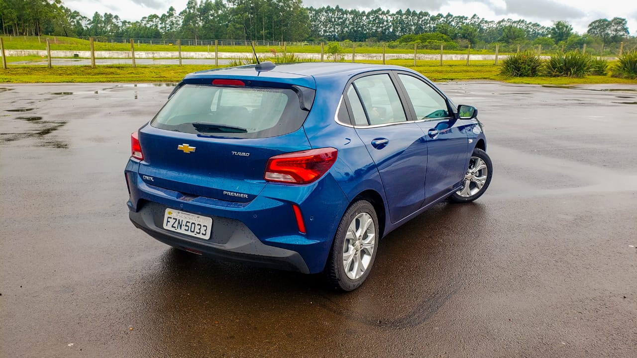 Chevrolet Onix Hatch azul de traseira em uma pista úmida e ao fundo gramado verde