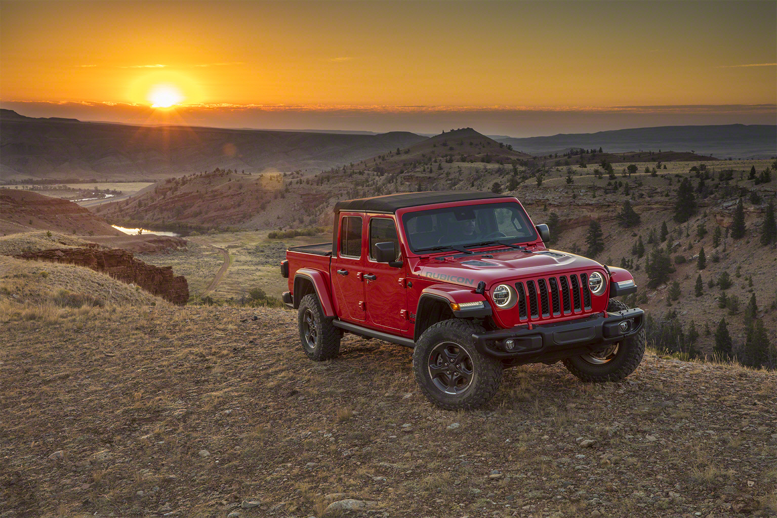 Jeep Gladiator vermelha de frente tendo ao fundo o pôr do sol do deserto
