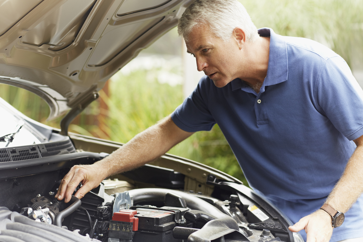 Homem mexe no compartimento do motor do carro, que está com o capô aberto