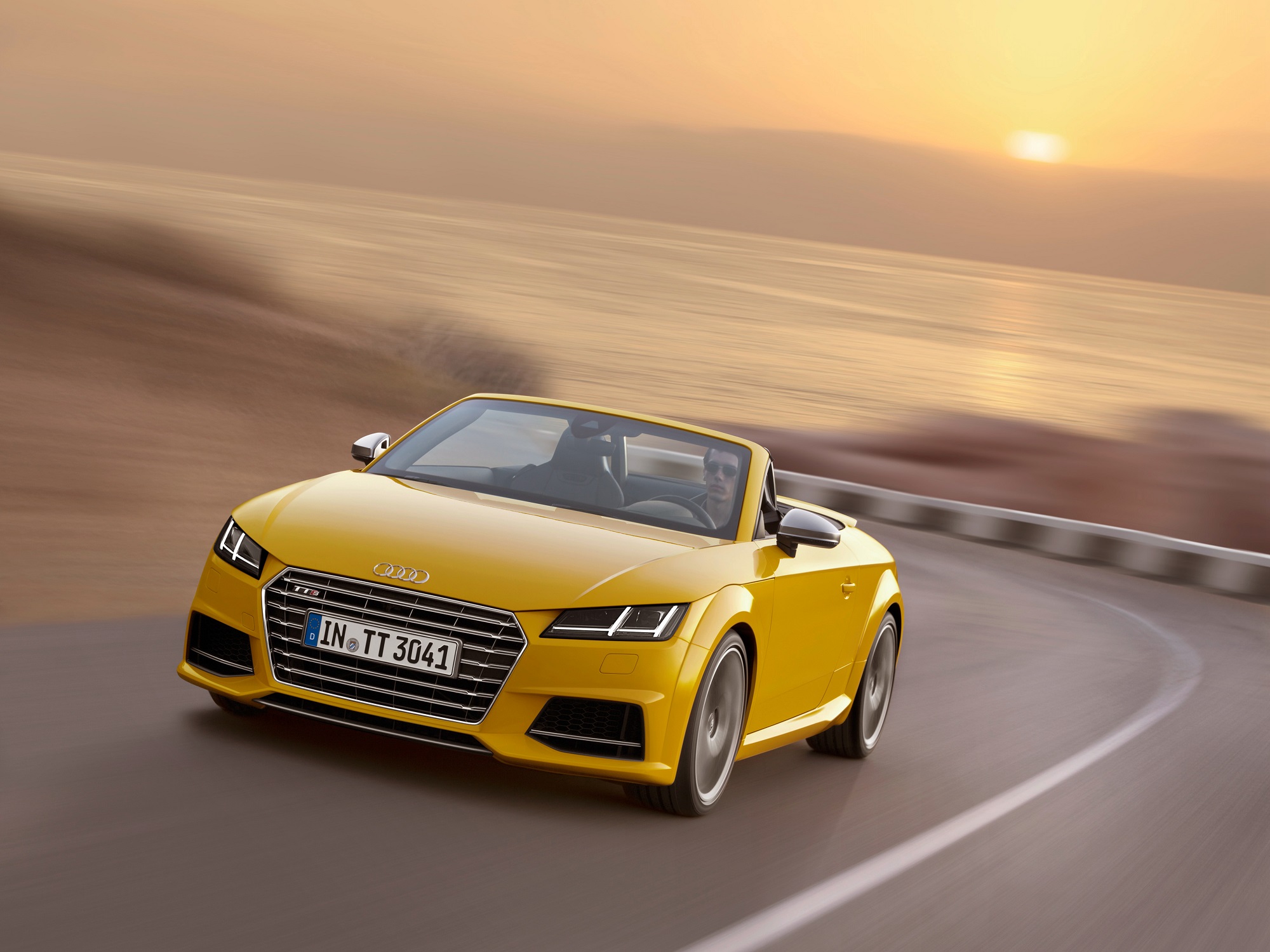 Audi Tt Roadster amarelo em movimento numa estrada de serra com o sol se ponto no horizonte ao fundo