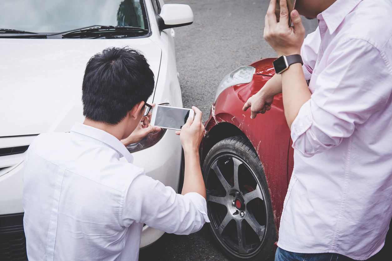 Dois homens observam dois carros que colidiram levemente para choque com paralama