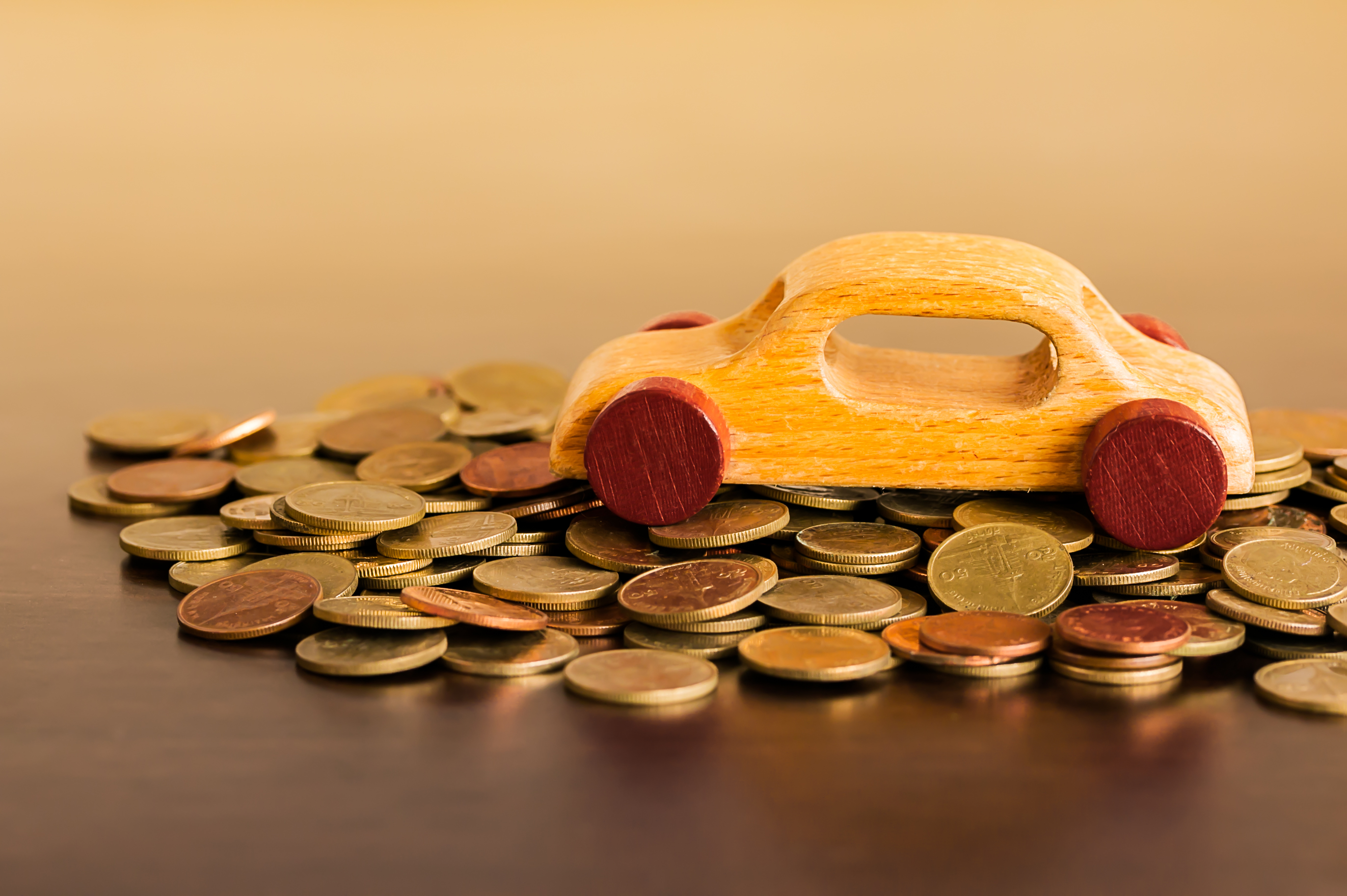 Imagem de um carro de madeira de brinquedo em cima de uma pilha de moedas