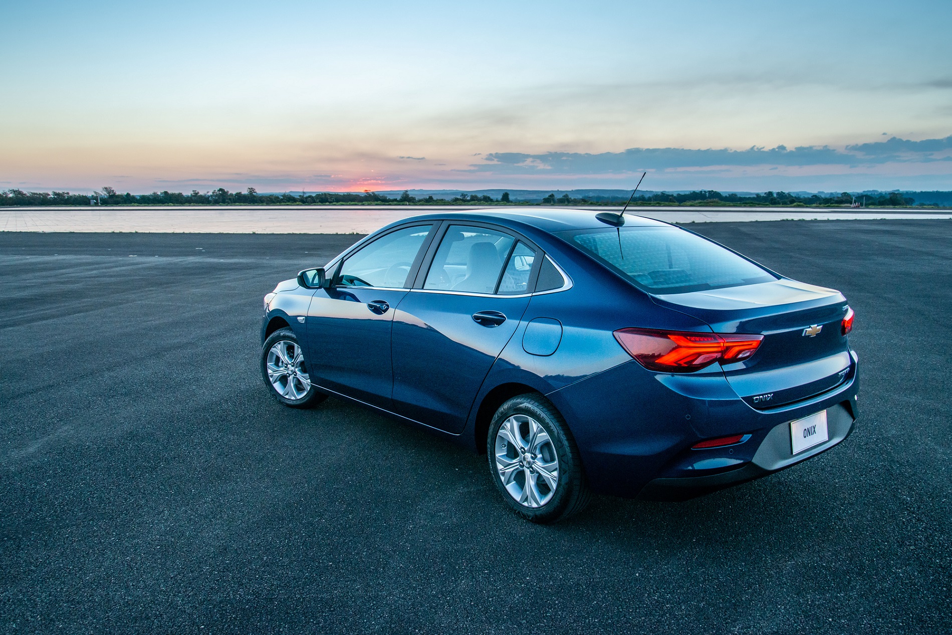 Chevrolet Onix Plus Premier na cor azul escuro de traseira com as lanternas que invadem as laterais e, ao fundo, uma paisagem natural