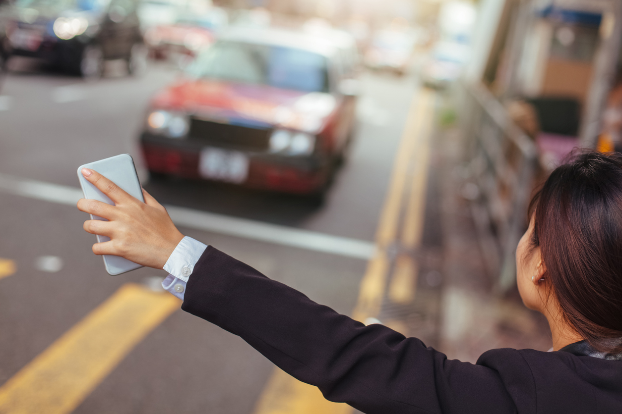 Mulher na rua com celular na mão chama carro de aplicativo