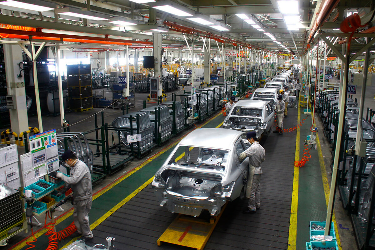 Linha de produção de automóveis na China mostra funcionários com máscaras trabalhando em uma arquitetura de carro
