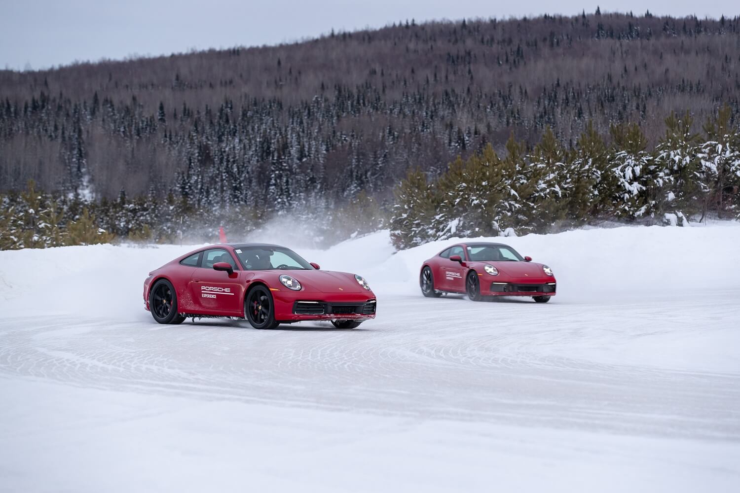Dois Porsche 911 vermelhos deslizam em uma curva de gelo
