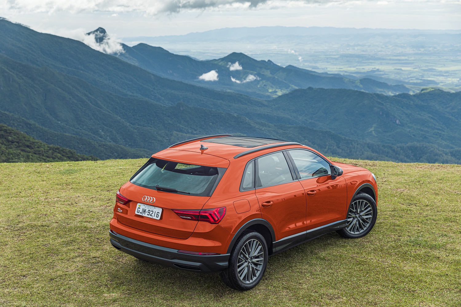 Audi Q3 laranja de traseira visto de cima estacionado sobre a grama com um vale ao fundo