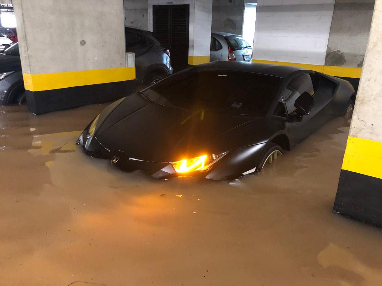 Foto mostra Lamborghini Huracán preto na garagem com água acima das rodas e da placa