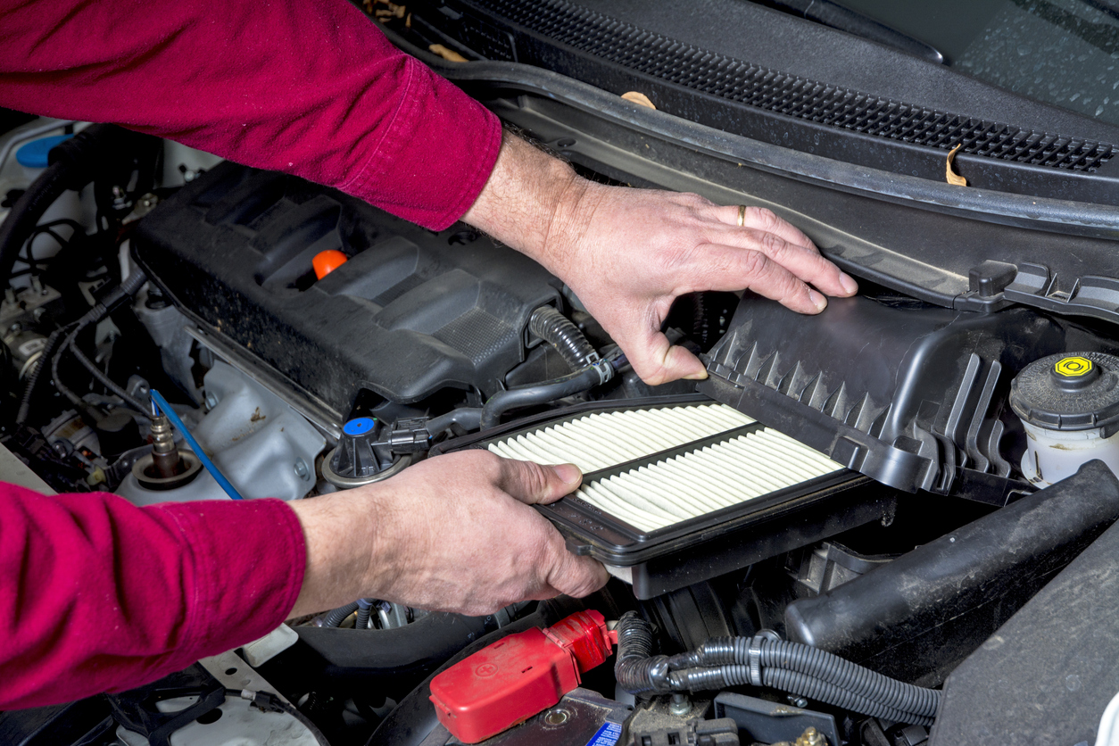 Homem checa o filtro de ar dentro do compartimento do motor do carro