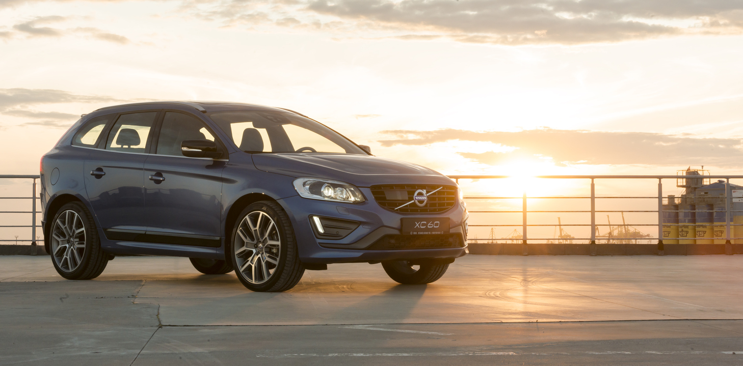 Volvo XC60 azul na diagonal ambientado em cenário natural ao por do sol