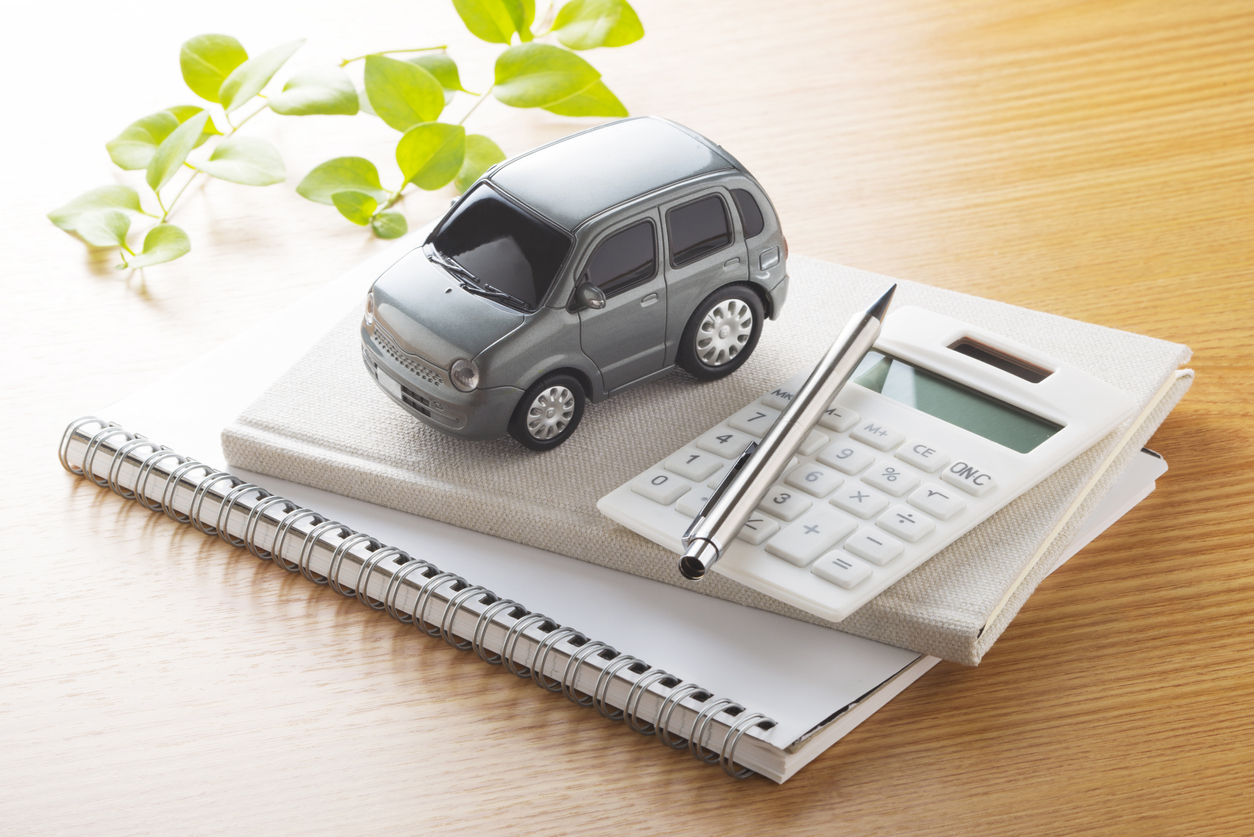 carrinho de brinquedo cinza ao lado de calculadora branca e, ambos, em cima de um pequeno caderno de anotações