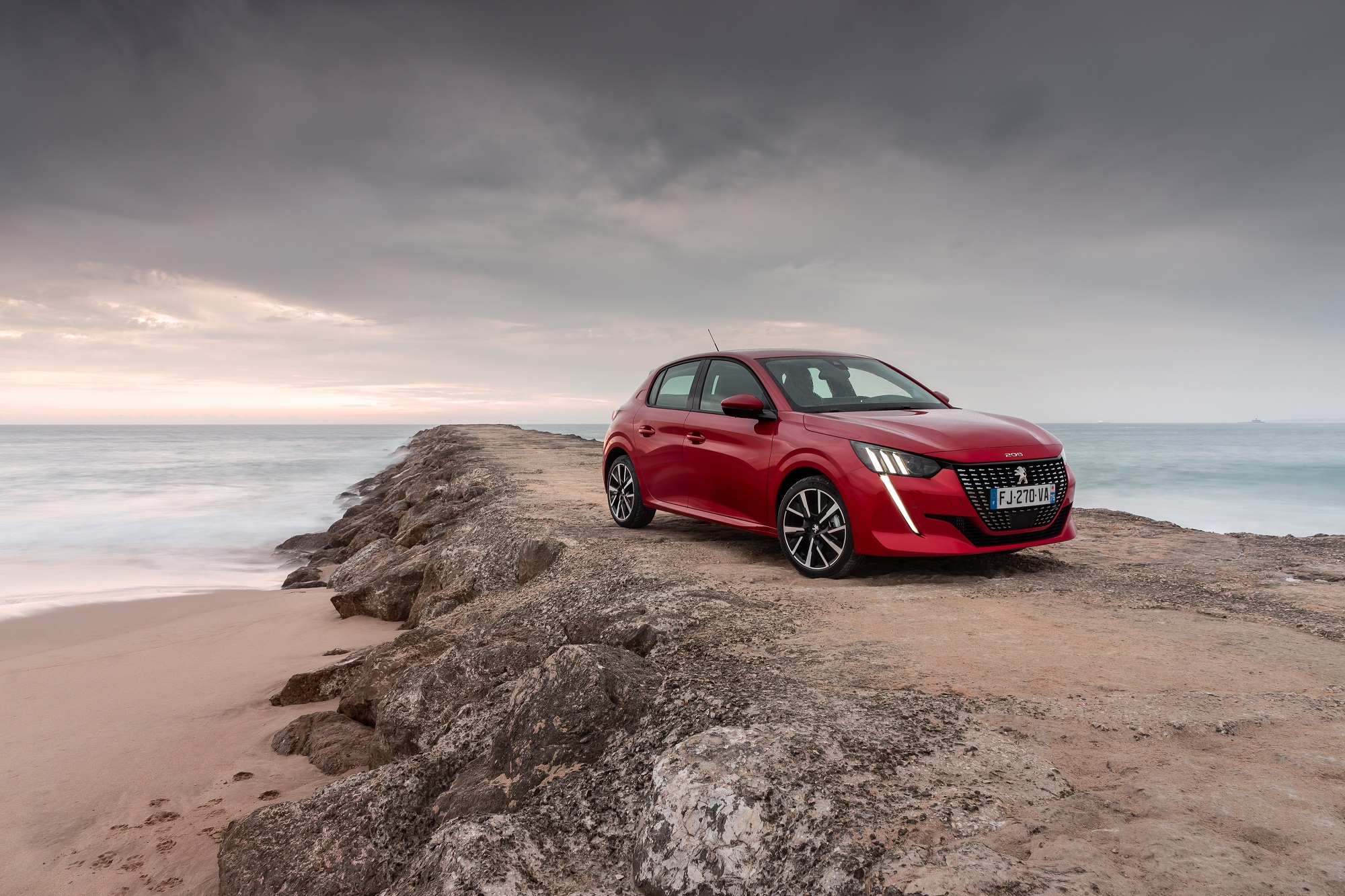 Novo Peugeot 208 na cor vermelha no alto de uma pedra em uma praia