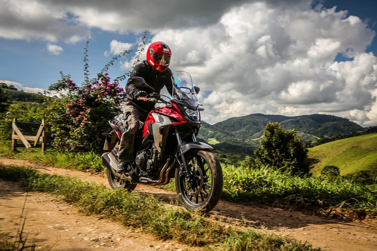 Honda CB 500X sendo pilotada na terra tem tanque vermelho