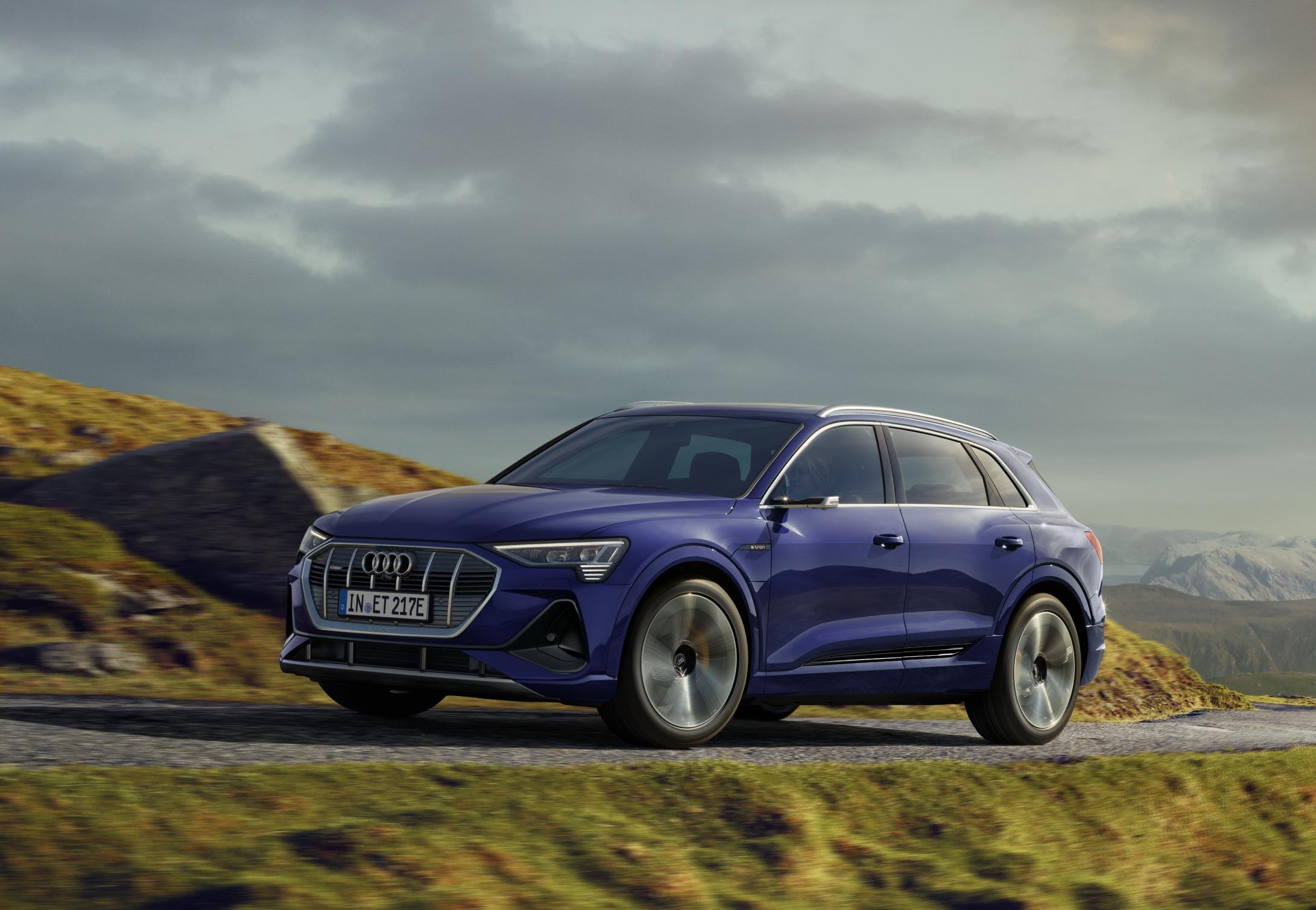 Audi E Tron azul em movimento numa curva em uma estrada na montanha