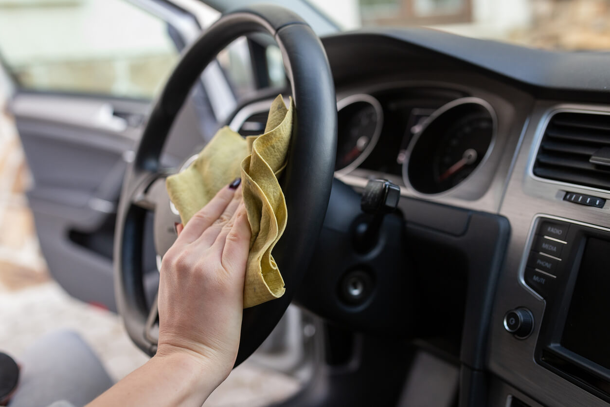 Mão de mulher aparece limpando o volante de um carro com um flanela