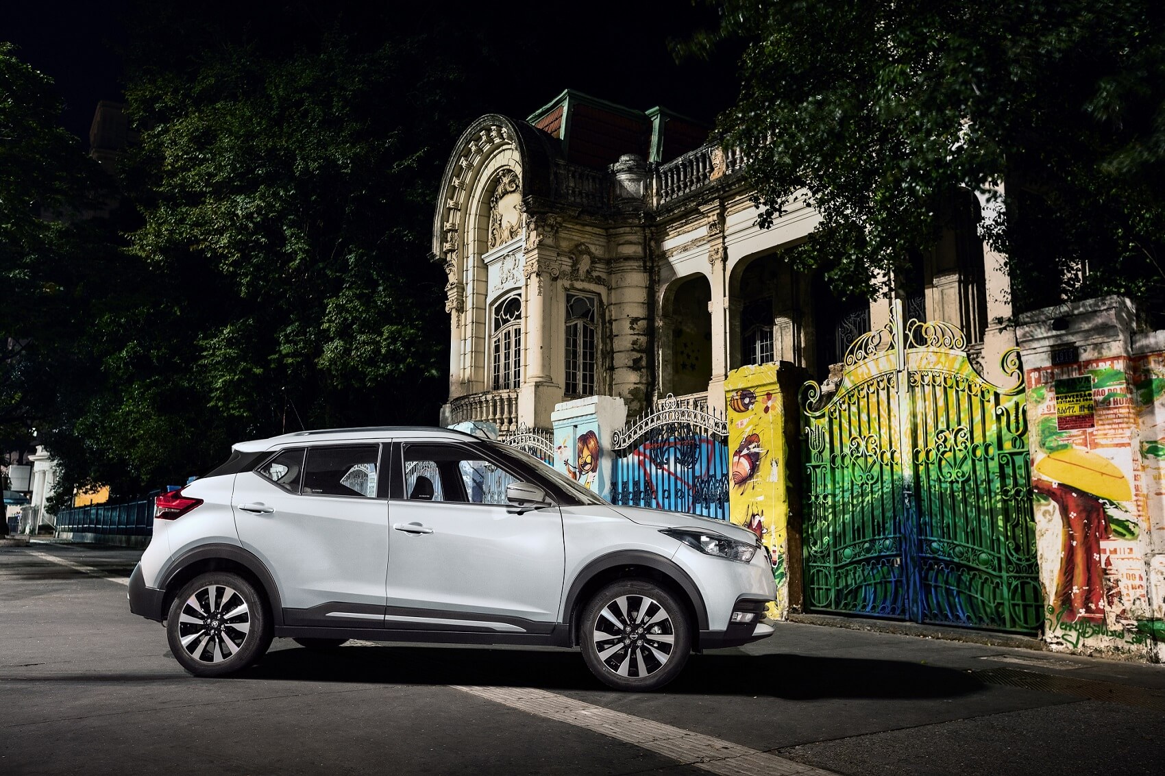 Nissan Kicks branco de perfil em frente a um portão e muro grafitados