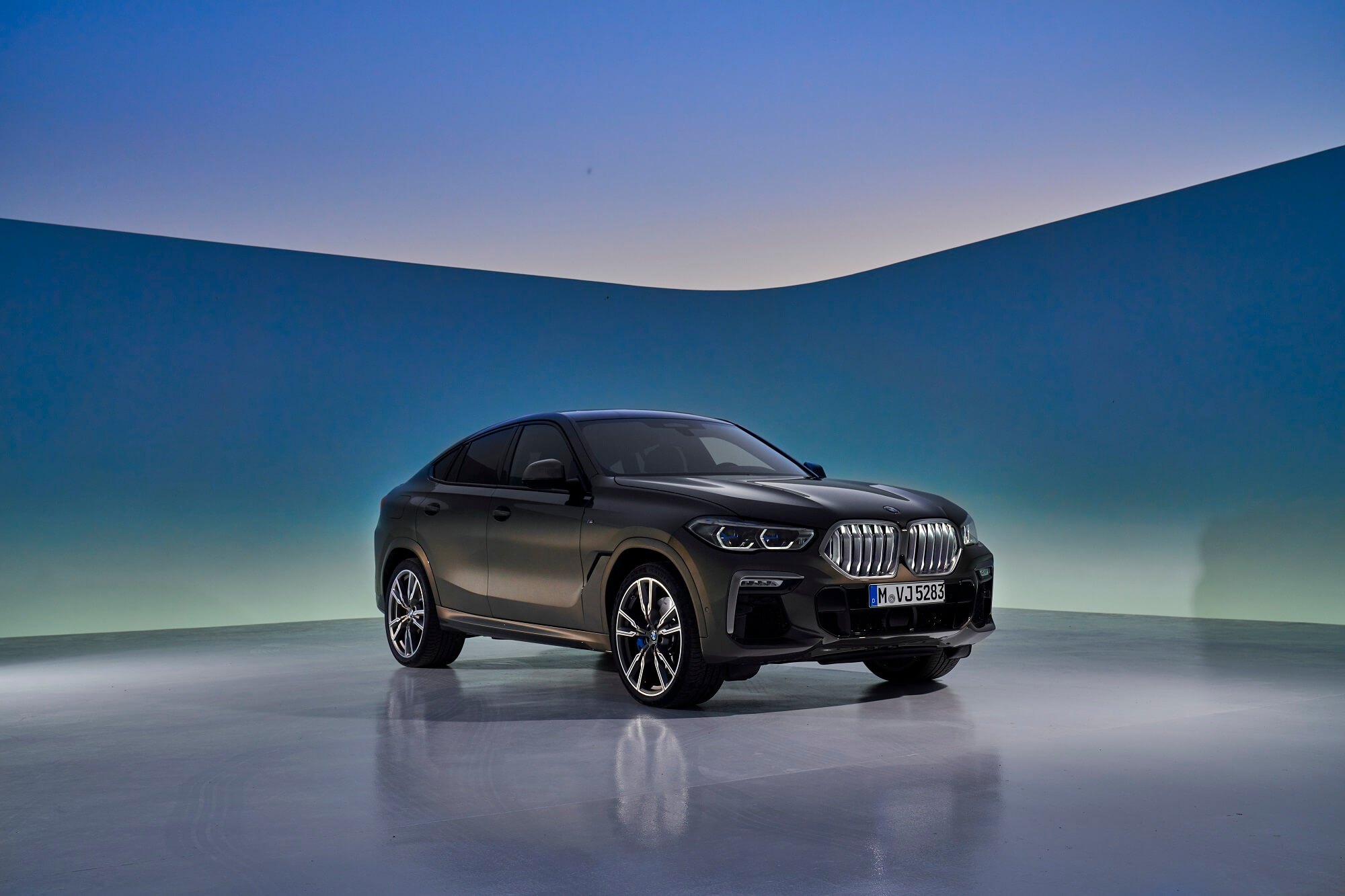 Bmw X6 de frente em estído com iluminação no chão e fundo azul