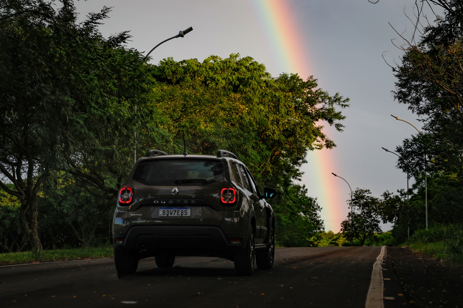 Novo Renault Duster de traseira em movimento na estrada com um arco-íris no horizonte da rodovia