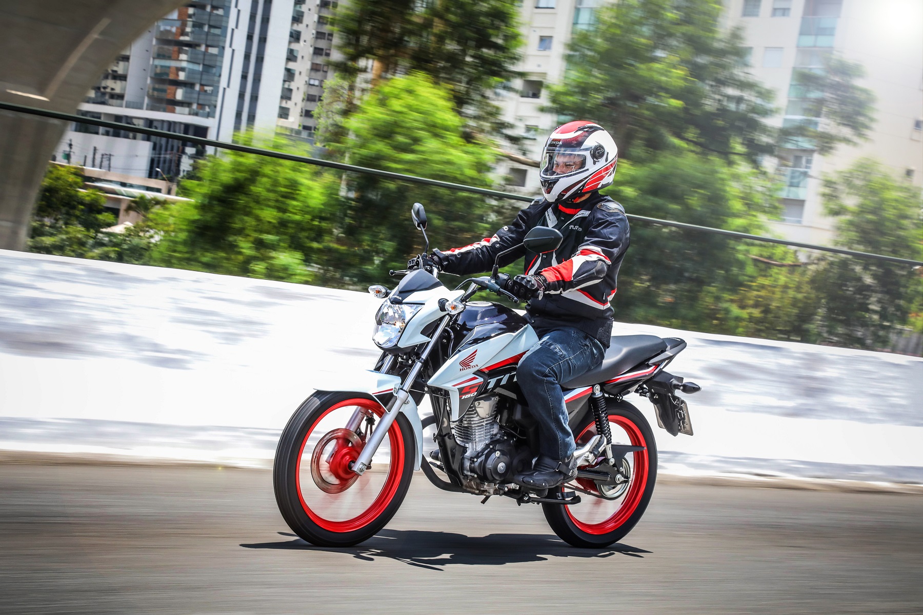 Honda CG 160 Titan na cor branca com grafismos no tanque vermelhos e rodas vermelhas em movimento em um viaduto