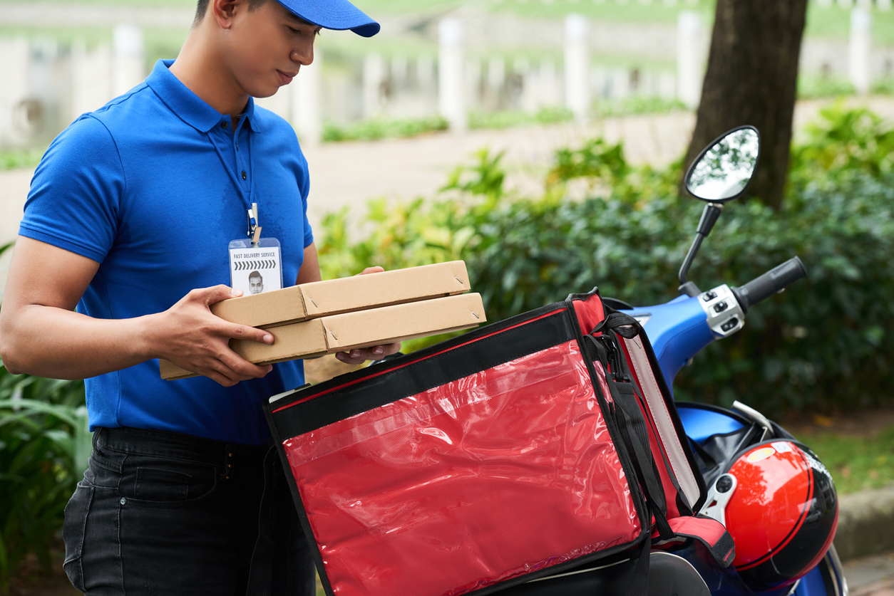 Entregador de aplicativo verifica caixas de pizza em cima do box instalado na motocicleta