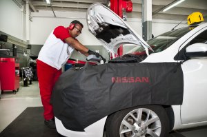 Carro da Nissan com capô levantado dentro da oficina e com profissional fazendo reparos