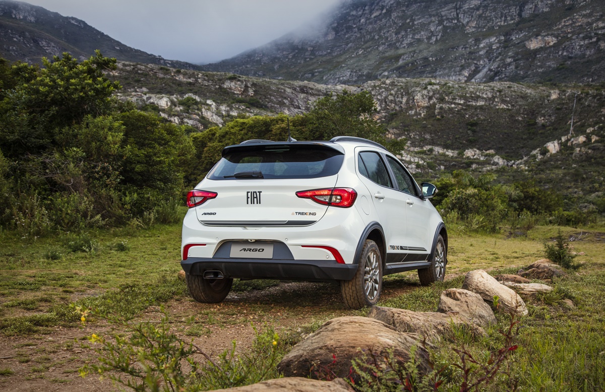 Fiat Argo Trekking de traseira em um gramado com algumas pedras e montanhas encobertas por nuvens ao fundo