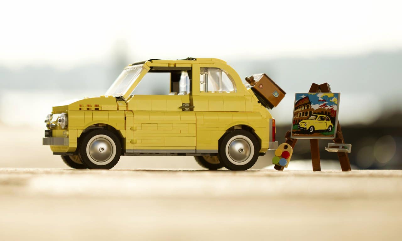 O Fiat 500 amarelo de miniatura da Lego montado com um pequeno cavalete, paleta de cores e tela de pintura