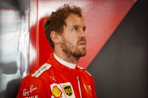 Foto mostra Sebastien Vettel com macacão da Ferrari olhando para o alto