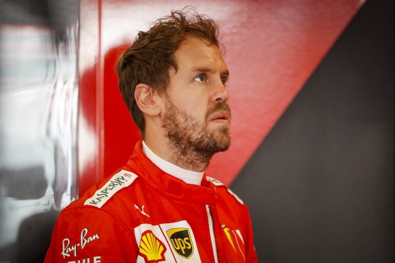 Foto mostra Sebastien Vettel com macacão da Ferrari olhando para o alto