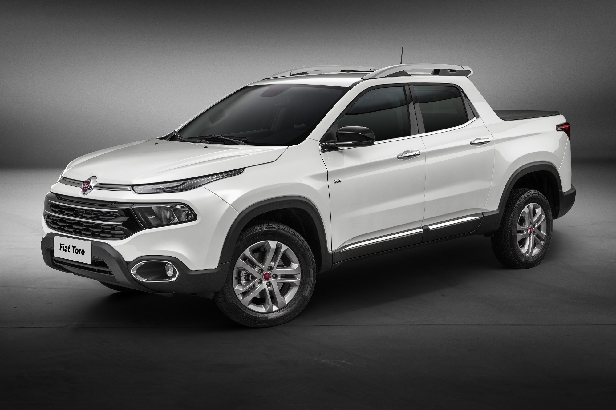 Fiat Toro branca na versão Volcano parada de perfil em estúdio com fundo cinza escuro