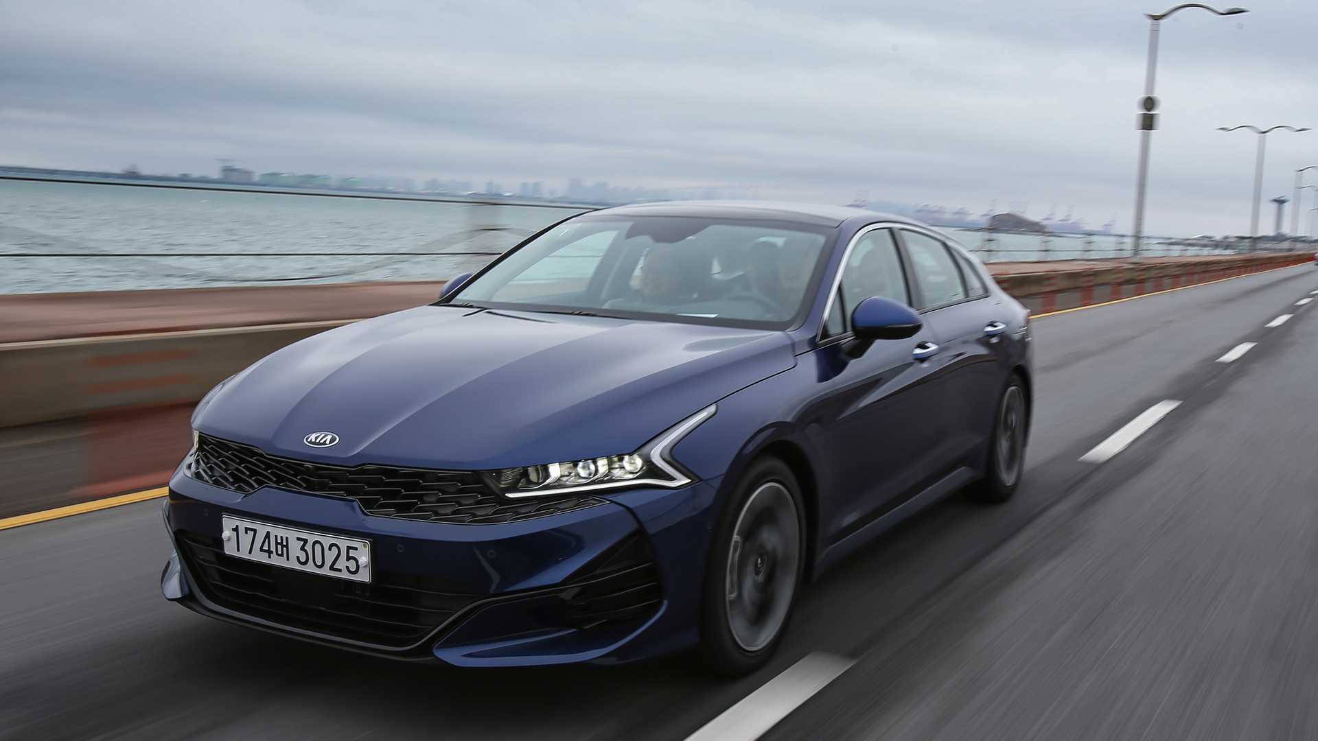 Kia Optima azul escuro em movimento na estrada com mar ao fundo