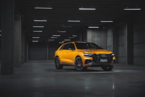 Audi Q8 dourado de frente em um estacionamento com piso cinza, pilastras ao fundo e luzes no teto