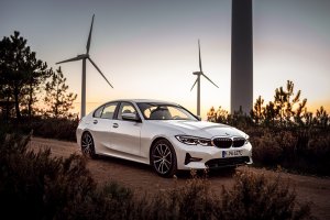 Bmw Série 3 branco em uma estrada com moinhos de energia eólica ao fundo no entardecer