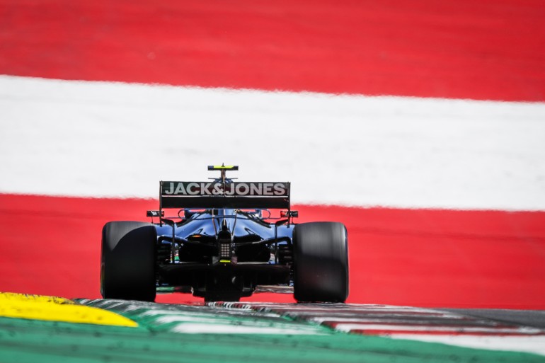 Carro de Fórmula 1 no Gp Da Áustria de 2019 tendo ao fundo um muro com a scores da bandeira vermelha e branca da Áustria