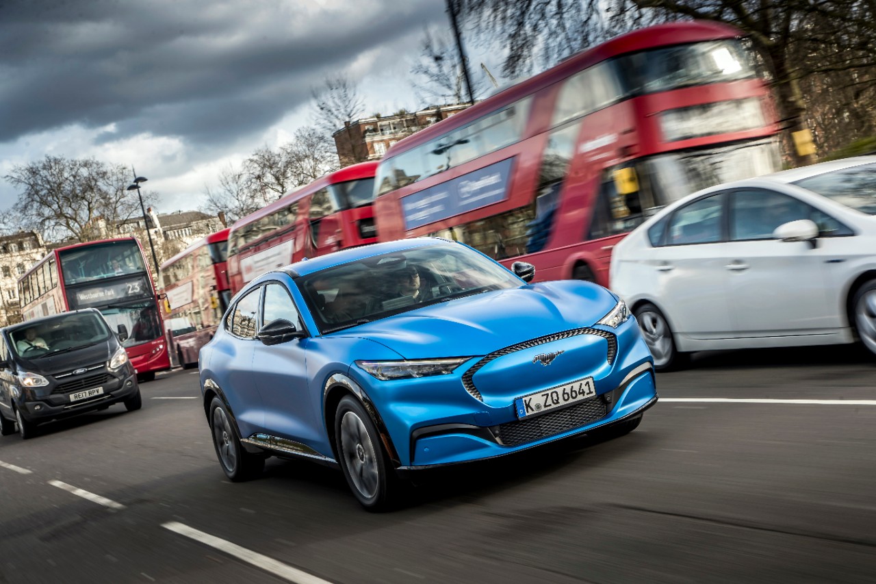 Mustang mach E azul em movimento em uma rua de Londres ao lado de um ônibus tradicional de dois andares