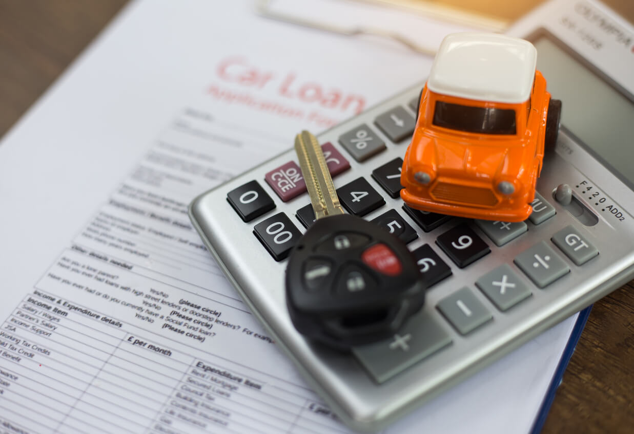 Imagem mostra uma miniatura de carro laranja e uma chave de automóvel em cima de uma calculadora prateada