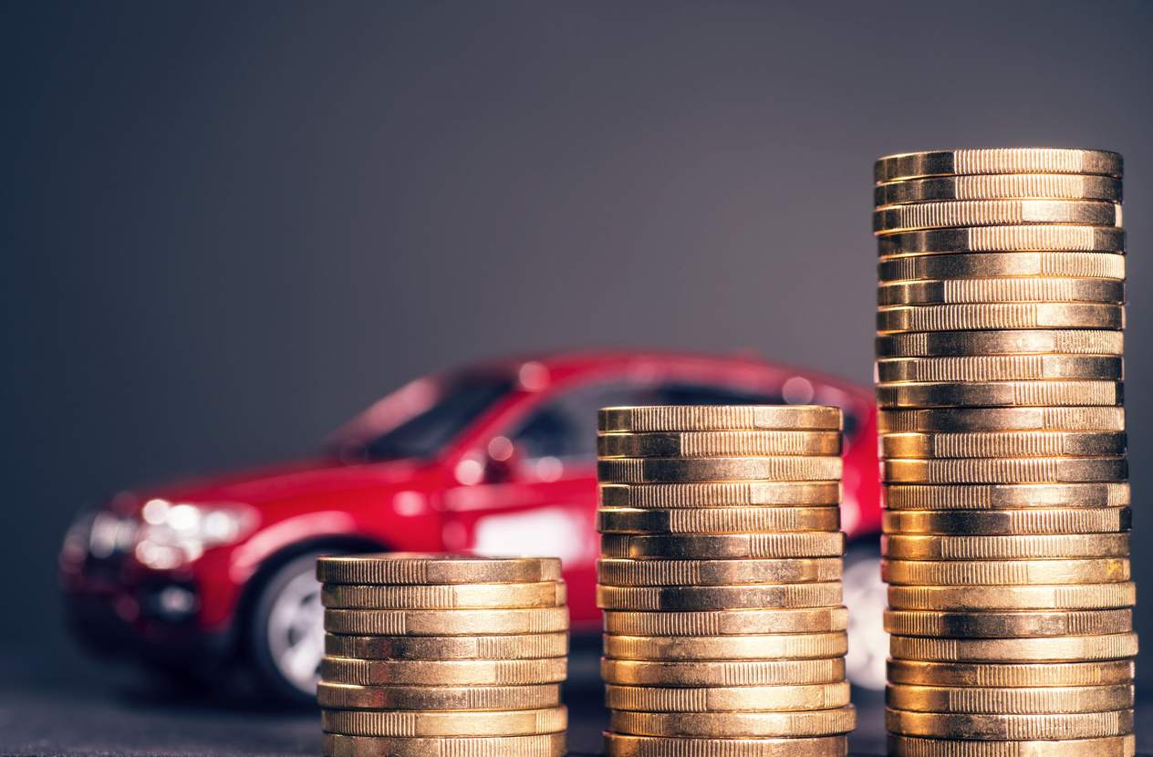 Imagem mostra pilha de moedas em primeiro plano com um carinho miniatura vermelho desfocado ao fundo para uilustrar omo economizar no seguro do automóvel?